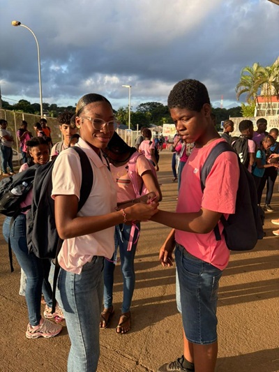 Une élève accroche un ruban rose au poignet d'une camarade à l'entrée du collège
